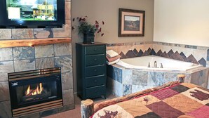 A bathroom with a fireplace, a large mirror, a bathtub, and a television mounted on the wall. - Fawn Valley Inn: 105 (Estes Park)