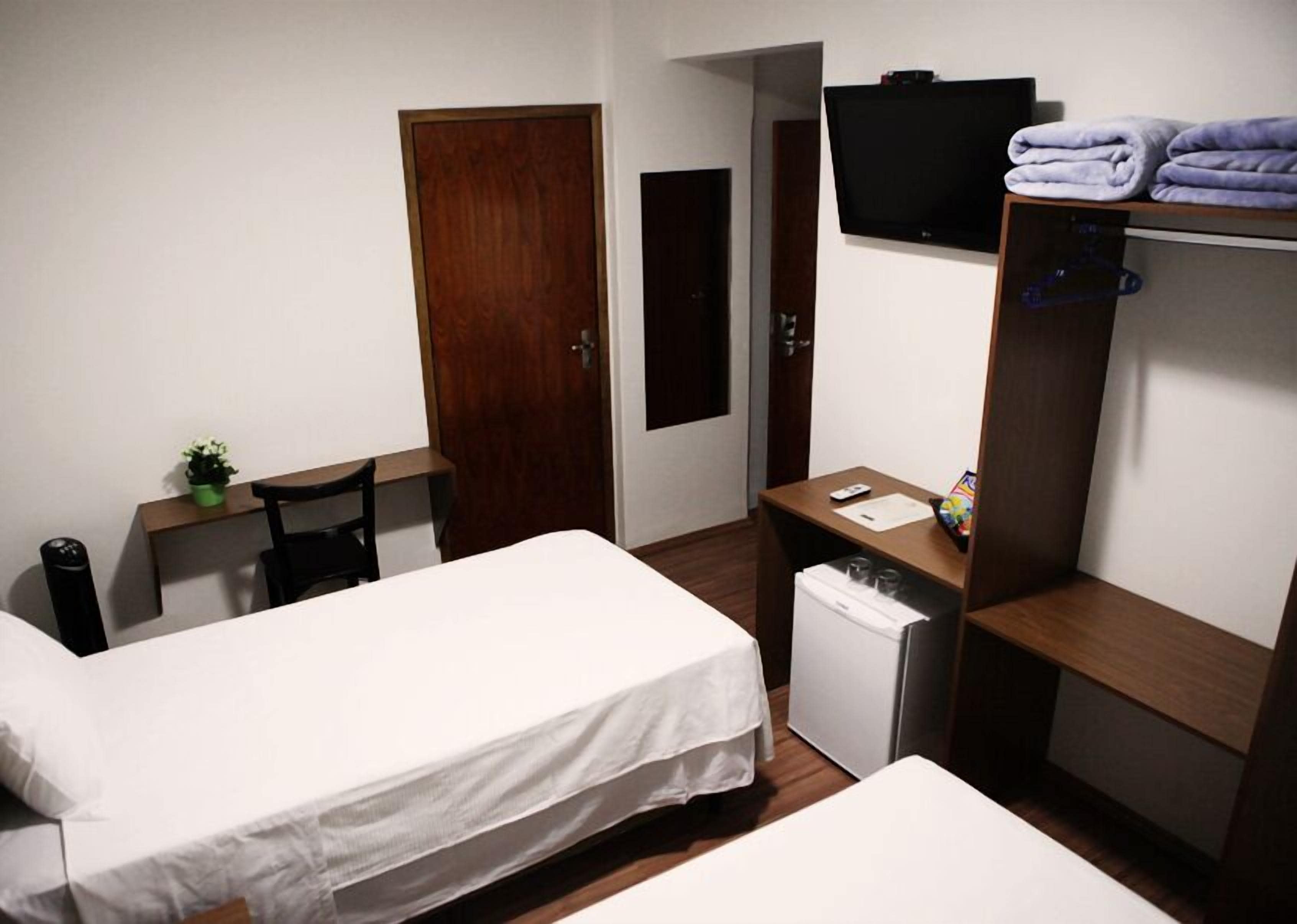 Habitación de hotel con dos camas, un escritorio, televisión, refrigerador pequeño y armario.