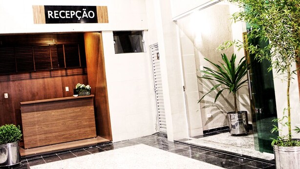 Un área de recepción con un mostrador de madera, plantas en macetas y un cartel que dice "RECEPCÃO".