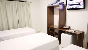 Habitación de hotel con dos camas individuales, un escritorio con silla, un refrigerador pequeño y un televisor montado en la pared.