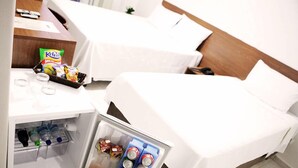 Habitación de hotel con dos camas, un minibar y una pequeña mesa con aperitivos y bebidas.