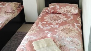 Un lit simple avec une couvre-lit à motifs floraux, deux oreillers, une couverture et un petit tapis sur le sol.