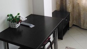 Une pièce avec une table noire, une petite plante blanche, un meuble noir et un rideau orné d’un motif doré.