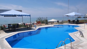 Piscina com vista para o mar, rodeada por espreguiçadeiras e guarda-sóis.