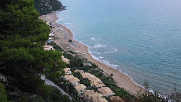 Uma área costeira com praia, casas e uma estrada.