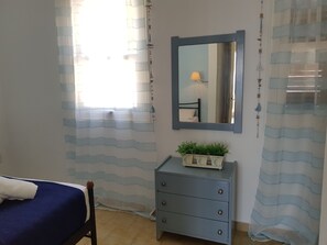 A bedroom with a bed, a dresser, a mirror, and a window with curtains.
