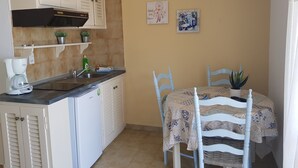 Cozinha compacta com cafeteira, pia e armários brancos. Há uma mesa de jantar com cadeiras e um vaso de planta.