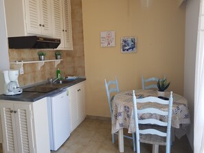 A compact kitchen with a coffee maker, sink, and white cabinets. There is a dining table with chairs and a potted plant.