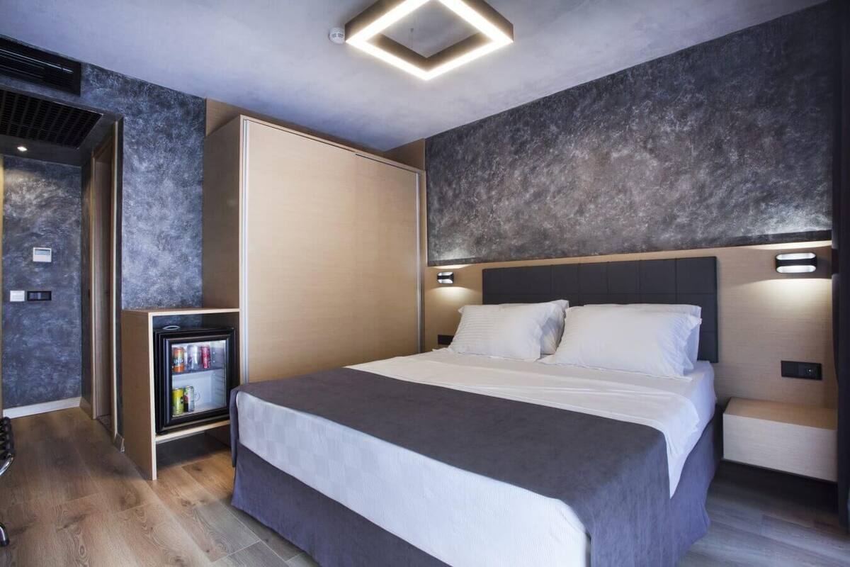 A modern hotel room with a large bed, a minibar, and a built-in wardrobe.