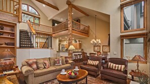 A spacious living area with a high ceiling, wooden staircase, and a dining area with a chandelier. - Luxe Arrowhead Home + Walk to Lift | Chalet Punto (Edwards)