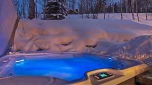 Ett bubbelbad med en digital kontrollpanel, omgivet av snötäckt mark och träd.
