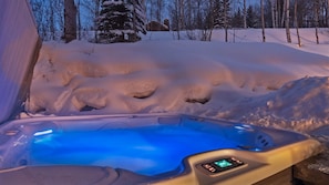Ein Whirlpool mit digitaler Steuerung, umgeben von verschneitem Boden und Bäumen.