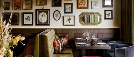 Un comedor con asientos tipo cabina, una mesa dispuesta para dos personas y una pared decorada con varias obras de arte enmarcadas.