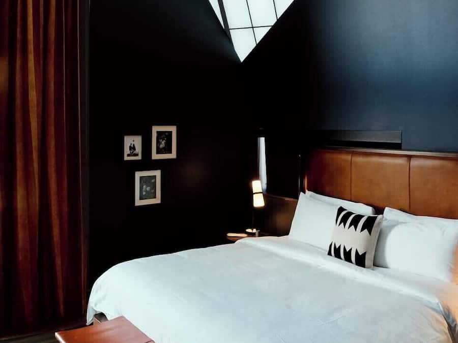 Une chambre d’hôtel moderne avec un grand lit, une lucarne et un banc en bois.