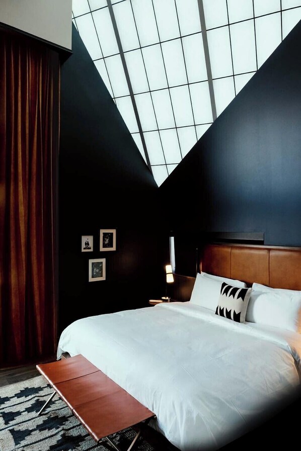 A modern hotel room with a large bed, a skylight, and a wooden bench.