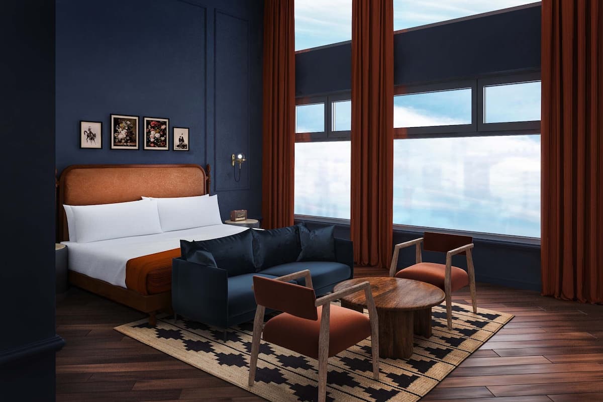 A modern bedroom with a large bed, a seating area with a coffee table, and a view of the city through large windows.