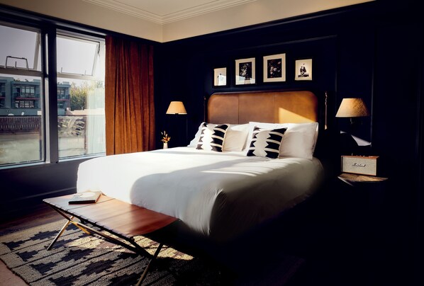 A hotel room with a large bed, two bedside tables with lamps, a window with curtains, and framed pictures on the wall.
