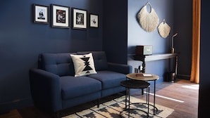Un salon moderne avec un canapé bleu foncé, un coussin décoratif à motifs, une petite table ronde et un élément décoratif fixé au mur.