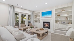 A modern living room with a fireplace, white furniture, and a large painting on the wall.