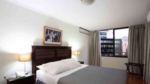 A hotel room with a large bed, a nightstand with a phone, a picture on the wall, and a window with curtains.