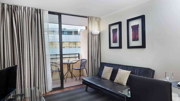 A modern hotel room with a glass door leading to a balcony, a sofa, a small table, and two framed pictures on the wall.