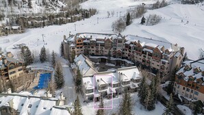 Een met sneeuw bedekte skigebied met meerdere gebouwen, waaronder een groot hotel en een skilift op de achtergrond.