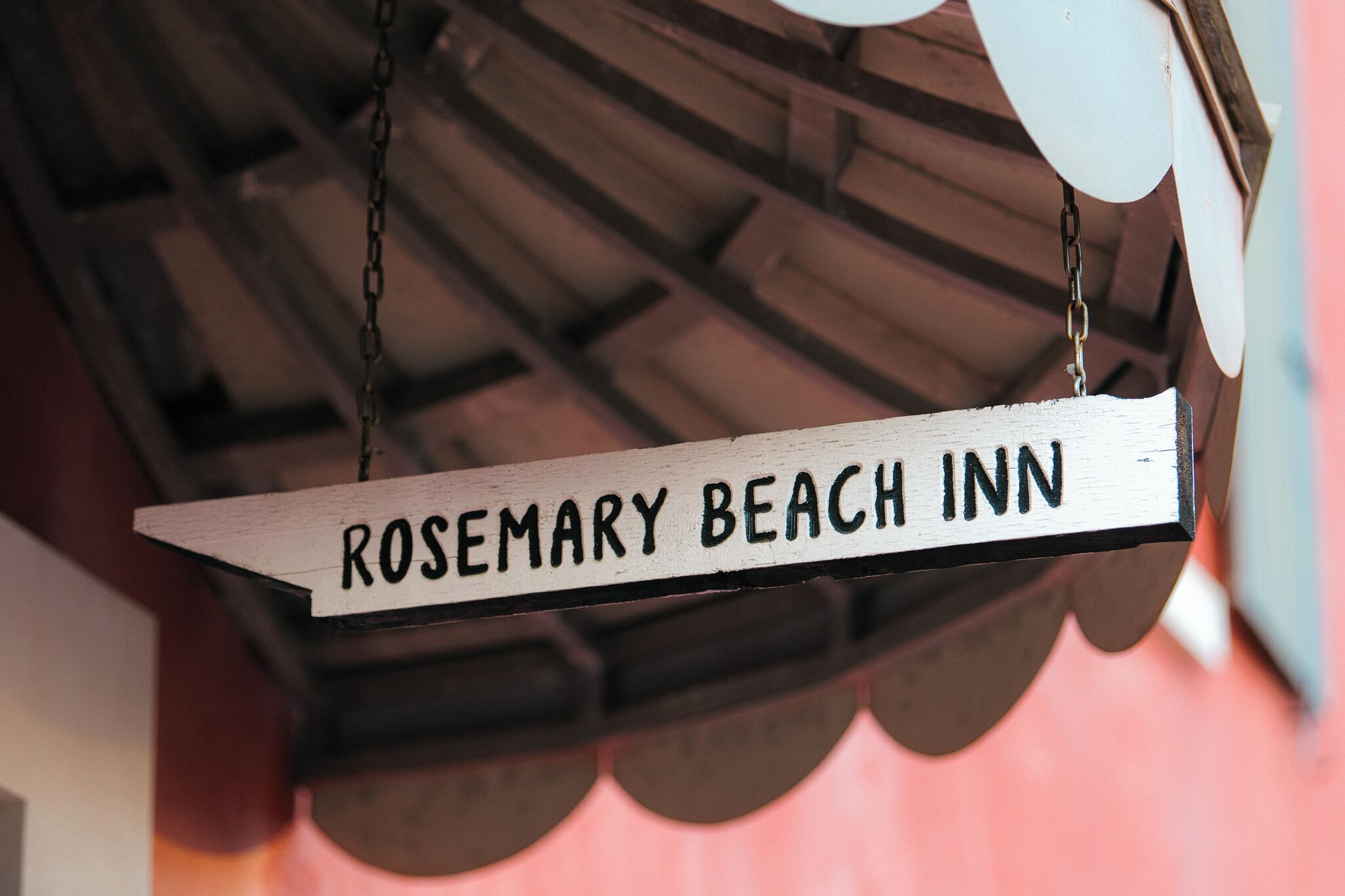 Une enseigne en bois portant l’inscription « ROSEMARY BEACH INN » est suspendue à une chaîne.