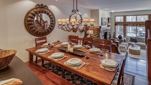 A dining room with a wooden table set for six, a chandelier, and a large mirror on the wall.