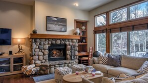 A cozy living room with a stone fireplace, a comfortable sofa, and a large window offering a view of trees.