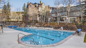 A swimming pool with a hot tub, surrounded by a stone wall and trees.