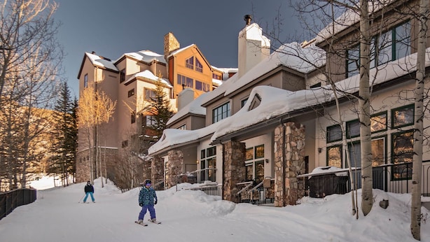 A snow-covered residential area with multi-story houses, a stone facade building, and a person skiing.