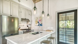 Een moderne keuken met een groot eiland, roestvrijstalen apparatuur en hanglampen.