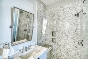 A bathroom with a large mirror, a sink, and a shower with mosaic tiles. - Enchanted Carriage House - Indoor/Outdoor Fireplace! Large Balcony! Free Bikes/Gym/Tennis! (Inlet Beach)