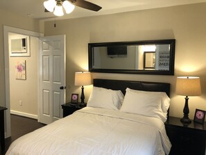 Cozy retreat with a neatly made bed, bedside tables, and a ceiling fan. A large mirror above the bed and framed decor add a personal touch.