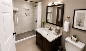 A bathroom with a shower, a sink, a toilet, a mirror, and a framed picture on the wall.