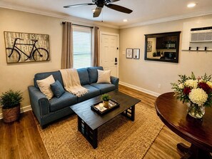 A living room with a sofa, coffee table, and a dining table with a vase of flowers.