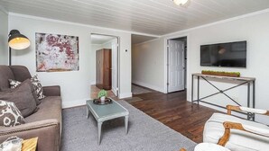 A living room with a sofa, coffee table, and a TV on a stand. - Downtown Bungalow by Mountain Oasis | Walking Distance to Downtown Square (Ellijay)