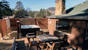 An outdoor patio with wooden furniture, a hot tub, and a stone building in the background. - Triple R Cottages: 1 (Estes Park)