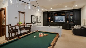 A living room with a pool table, a sofa, a TV, and a cabinet.