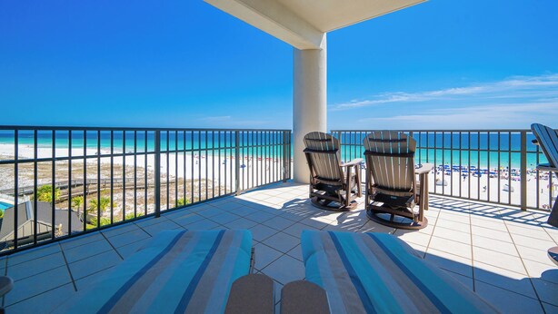 A balcony with two chairs and a table, overlooking a beach with a clear blue sky.