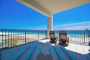 A balcony with two chairs and a table, overlooking a beach with a clear blue sky. - The Oasis at Orange Beach, formerly known as Phoenix West II, Unit 411 (Orange Beach)