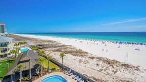 A beach resort with a pool, beach umbrellas, and a view of the ocean.