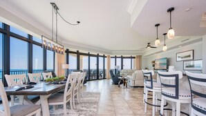 A spacious dining area with a high ceiling, large windows, and a view of the outdoors.