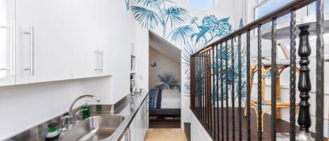 A modern kitchen with white cabinets, stainless steel appliances, and a black railing leading to a balcony with wicker furniture.