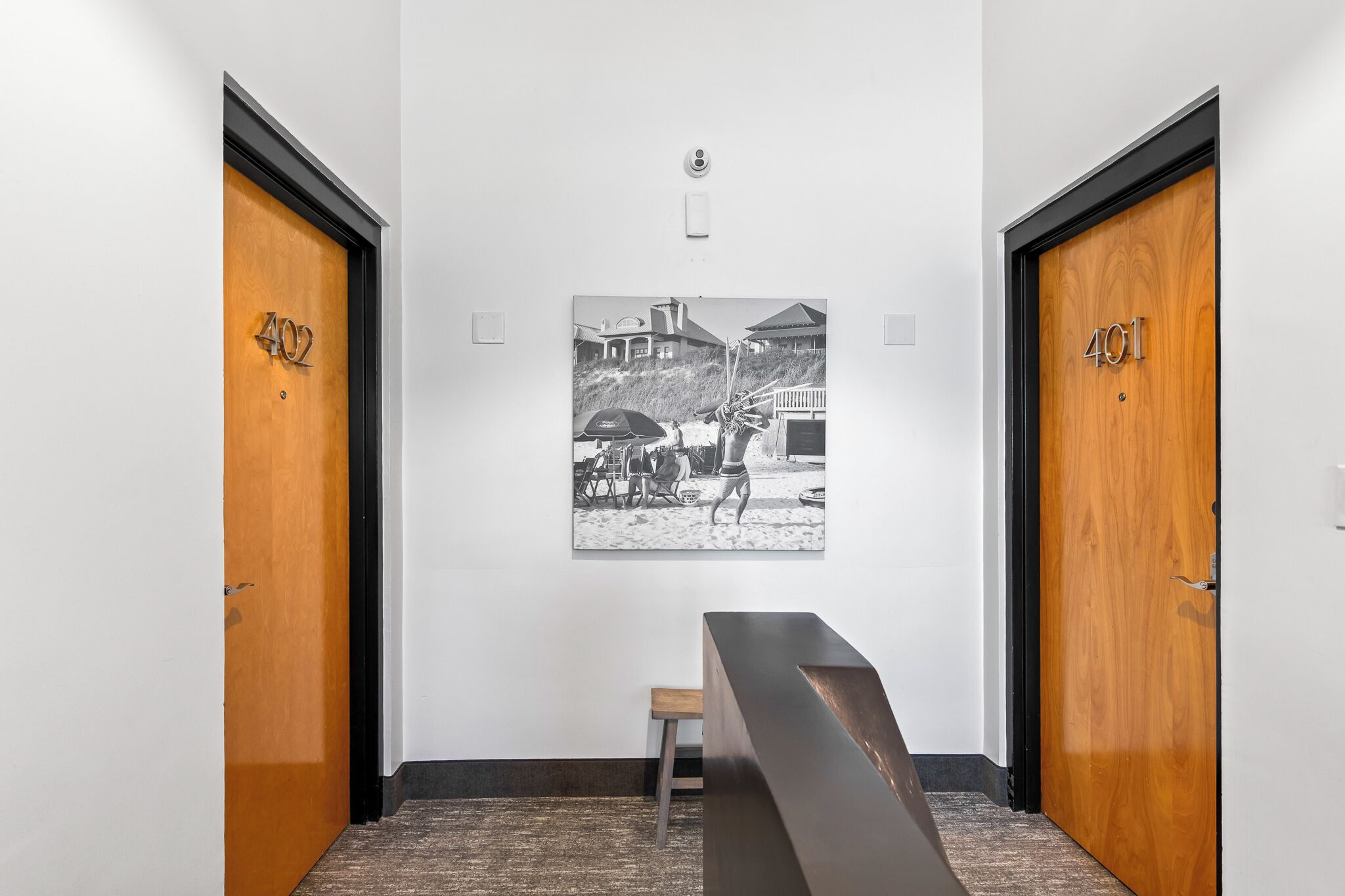 Un pasillo con dos puertas identificadas con los números 402 y 401, un banco y una fotografía blanco y negro en la pared.