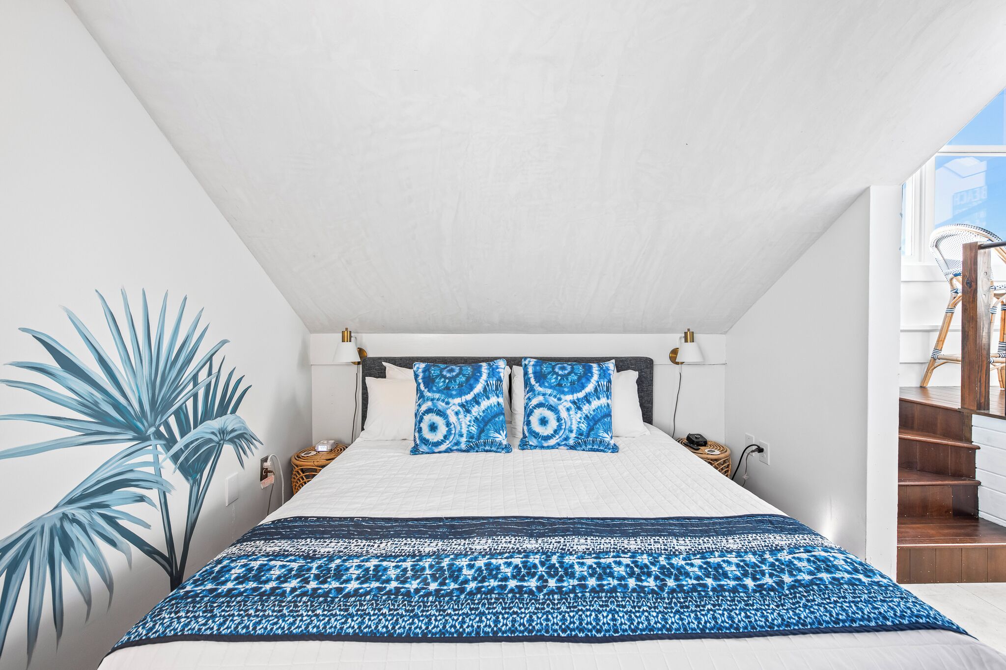 A bedroom with a large bed, two pillows, a bedside table, a lamp, and a plant.