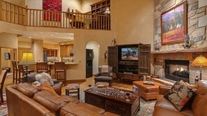 A spacious living room with leather sofas, a fireplace, a mounted TV, and a dining area with wooden furniture.