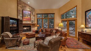 A cozy living room with a stone fireplace, leather furniture, and large windows offering a view of the outdoors.