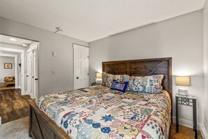 Quarto com cabeceira de madeira, colcha acolchoada, abajur e mesa de cabeceira.
