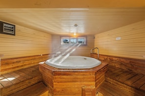 A wooden sauna with a large central tub, wooden benches, and a window providing a view outside.